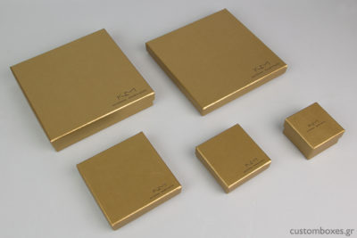 Κουτιά κοσμημάτων σε χρυσό χρώμα με τυπωμένο στο καπάκι το λογότυπο της σχεδιάστριας Κατερίνας Μακρυγιάννη.
