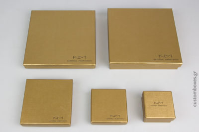 Κουτιά κοσμημάτων σε χρυσό χρώμα με τυπωμένο στο καπάκι το λογότυπο της σχεδιάστριας Κατερίνας Μακρυγιάννη.